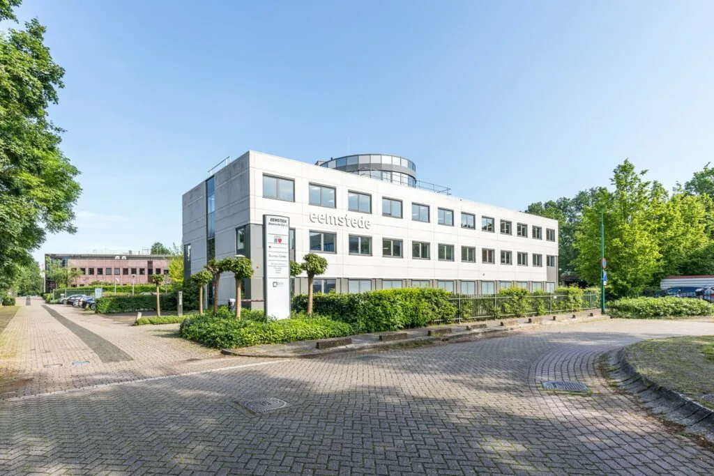 Modern kantoorgebouw "Eemstede" aan de Baarnsche Dijk met parkeerplaats en omliggend groen.